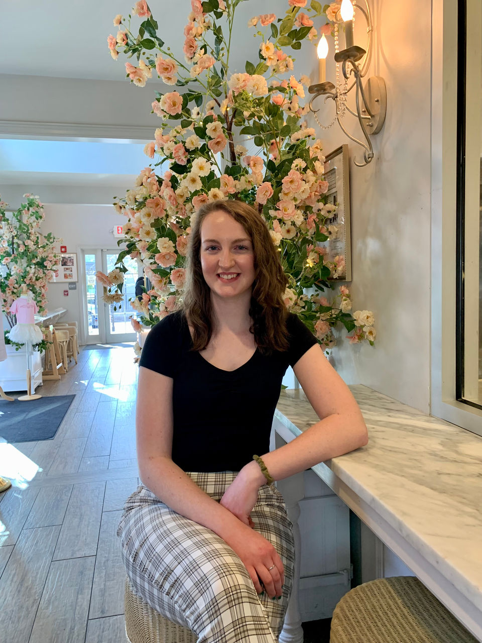 Graduate student Julie Schlanz poses on a stool with a large floral display behind her.