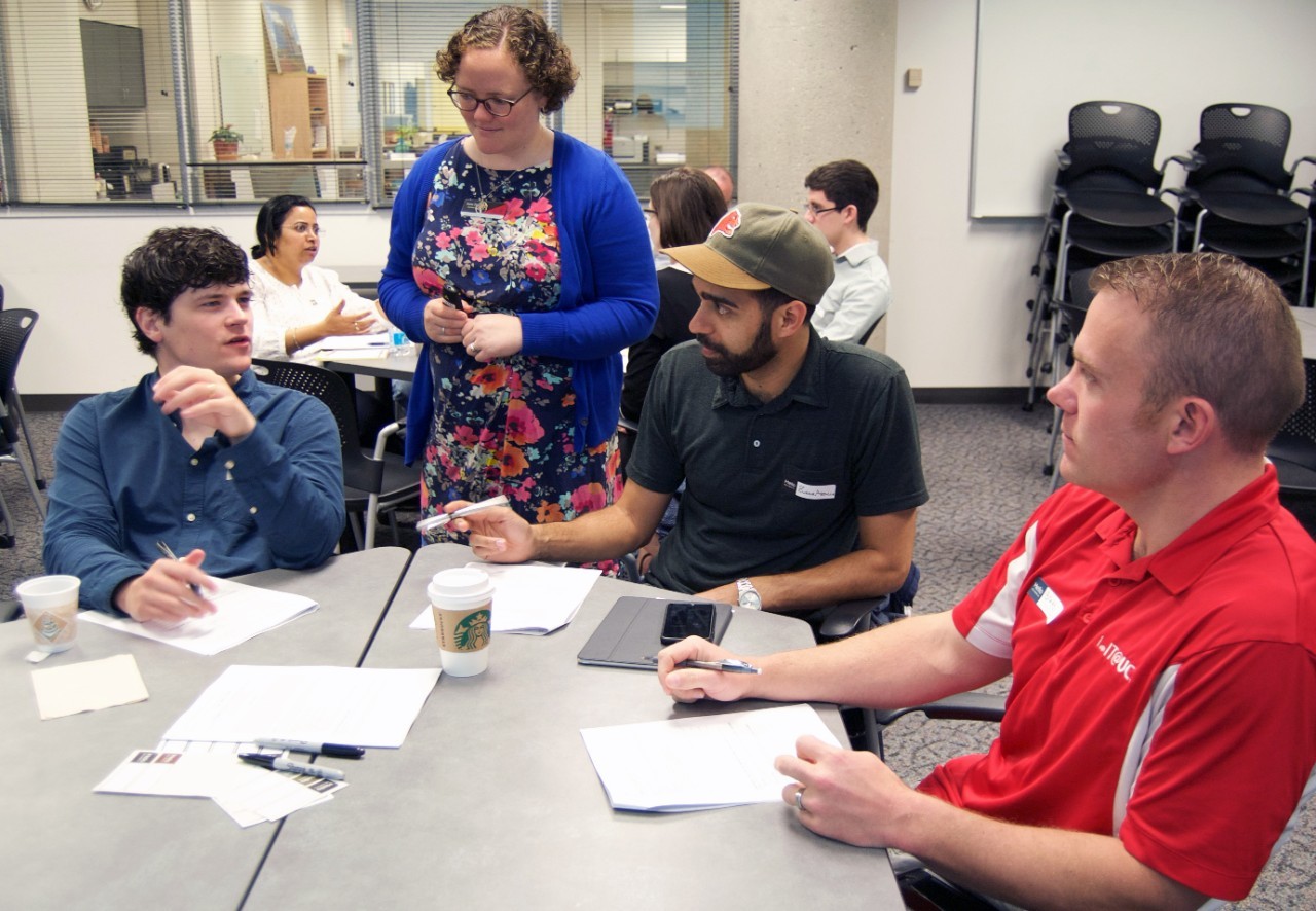 An instructor talks to three students sitting at a table. 