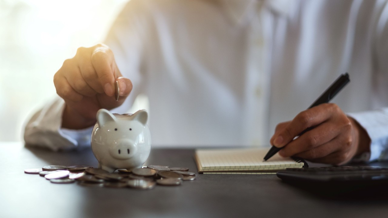 Person putting coins into a piggy bank. 